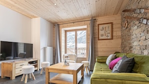 A cozy living room with a wooden ceiling, a green sofa, a wooden coffee table, a TV, and a stone wall. - Le Temps Suspendu "Chardon Bleu" - Relaxation Stay - Apartment 8 people (TERMIGNON)