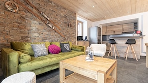 A cozy living room with a green sofa, wooden coffee table, and a stone wall. - Le Temps Suspendu "Chardon Bleu" - Relaxation Stay - Apartment 8 people (TERMIGNON)