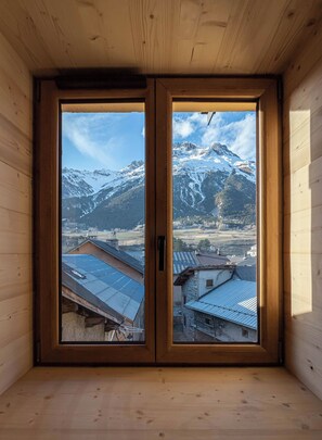 A wooden room with a large window offering a view of snow-capped mountains and a village below. - Le Temps Suspendu "Chardon Bleu" - Relaxation Stay - Apartment 8 people (TERMIGNON)