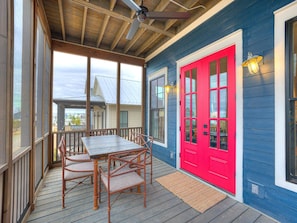 A covered porch with a table and chairs, a red door, and a view of the surrounding area.