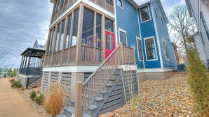 A two-story house with a prominent balcony, a red door, and a wooden staircase leading to the entrance.