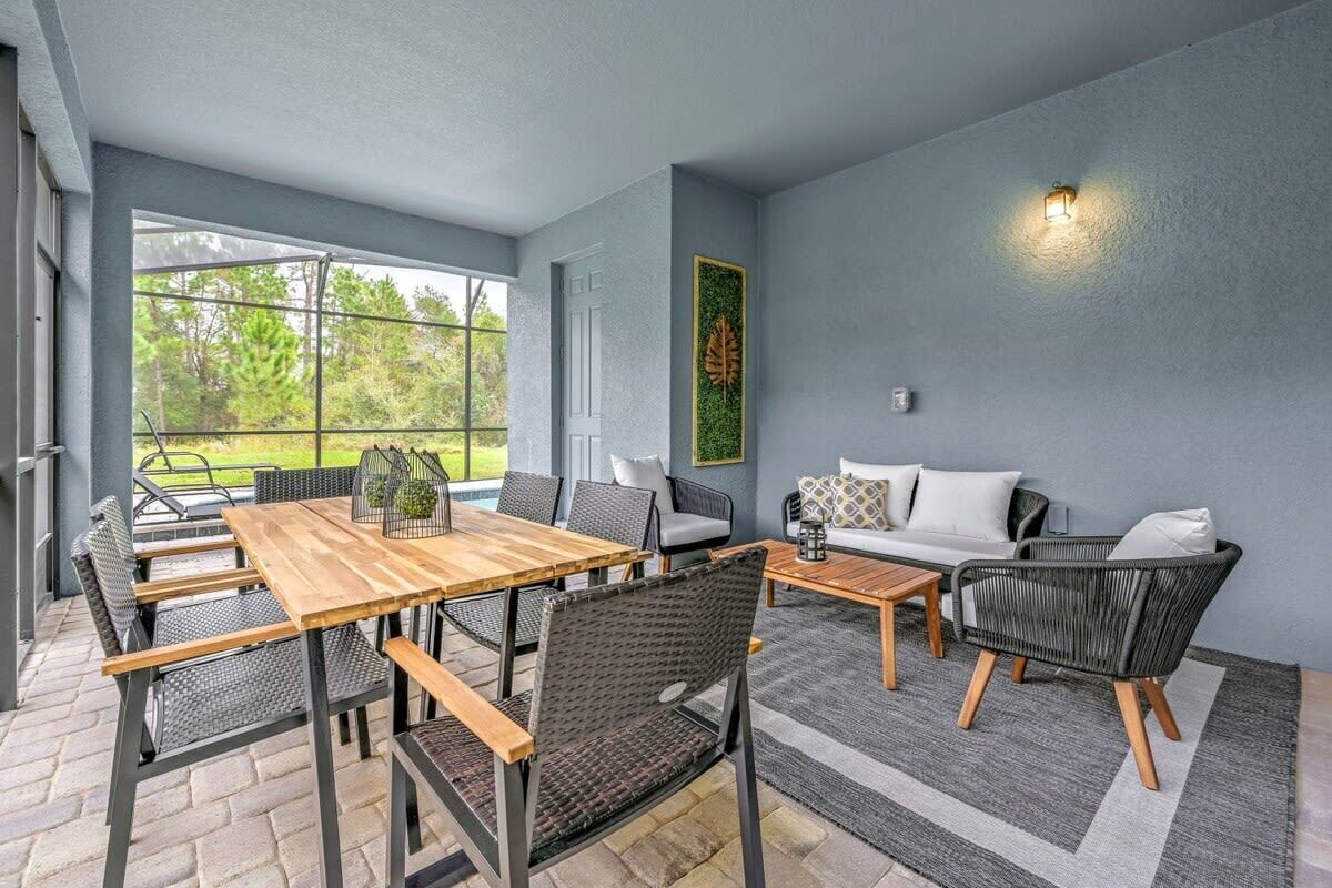 Ett modernt utomhusområde med sittplatser, bestående av ett tr äbord och stolar, en soffa och en dekorativ väggdekoration.