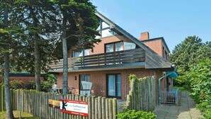 A two-story building with a sloped roof, a brick facade, and a wooden fence. - Appartement in Westerland auf Sylt (Westerland)
