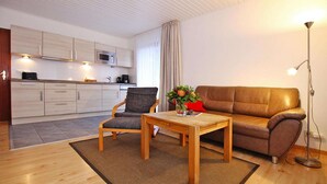 A modern living room with a sofa, armchair, coffee table, and a small kitchen area in the background. - Appartement in Westerland auf Sylt (Westerland)