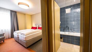 Habitación de hotel con cama, una silla, baño con bañera y vistas al exterior.
