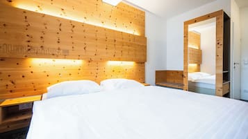 Una habitación de hotel con cabecera de madera, cama con ropa blanca, mesita de noche y armario.