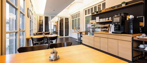 A modern cafe with wooden tables and chairs, a coffee machine, and shelves with items.