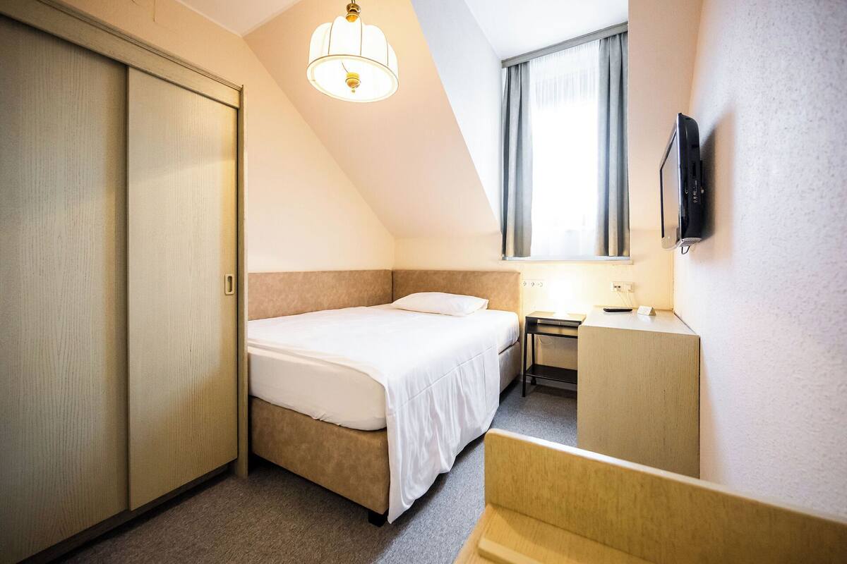 A hotel room with a bed, a desk, a chair, a TV, and a wardrobe.