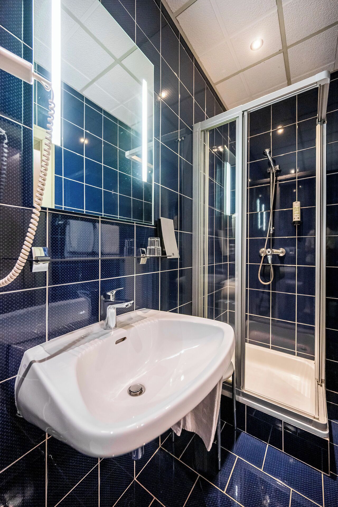 Un baño con un lavabo blanco, un espejo y una ducha con mampara de vidrio.