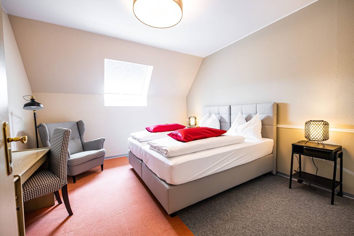 A bedroom with a bed, a chair, a desk, and a lamp.