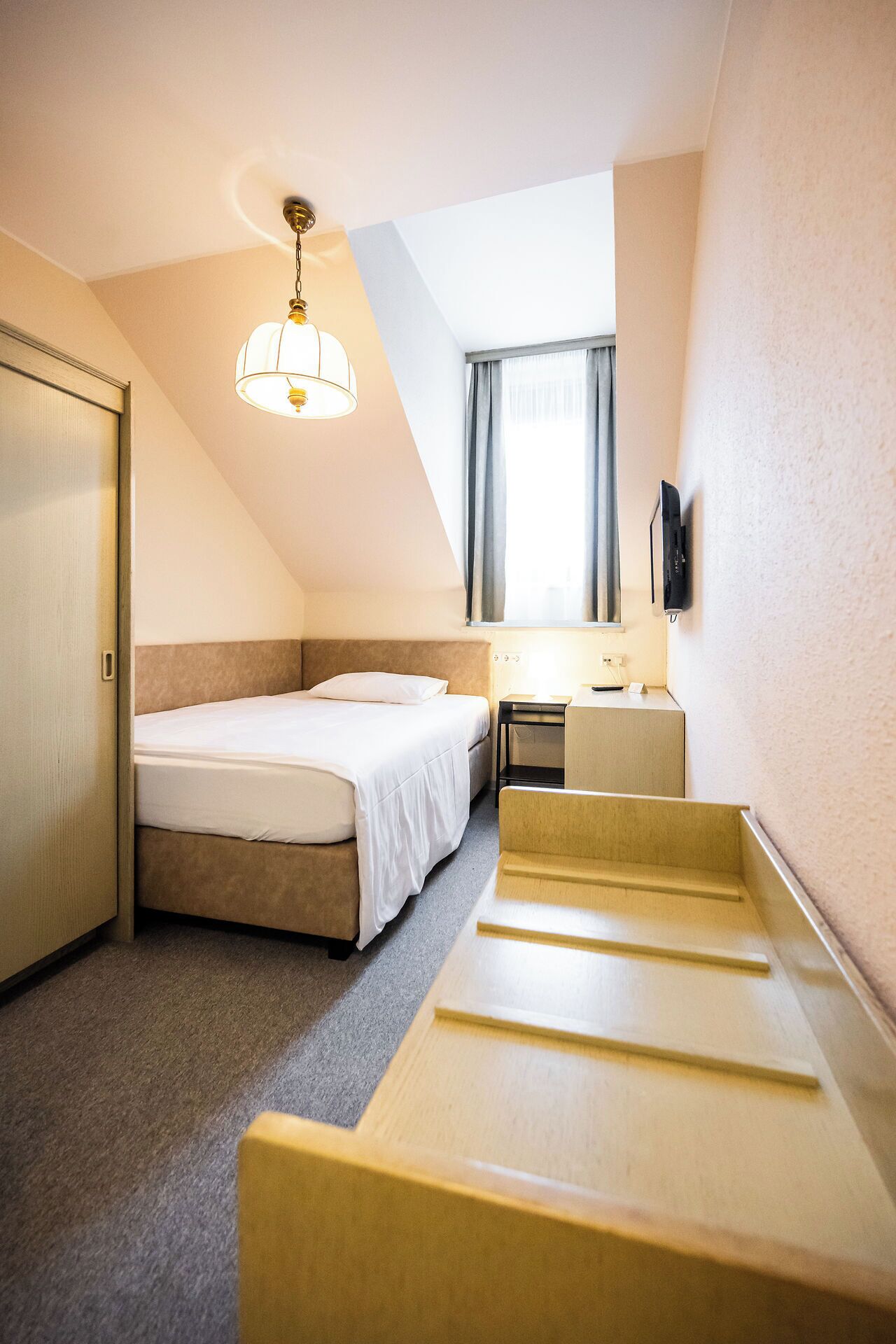 Una habitación de hotel con cama, escritorio, silla, televisor y luz en el techo.