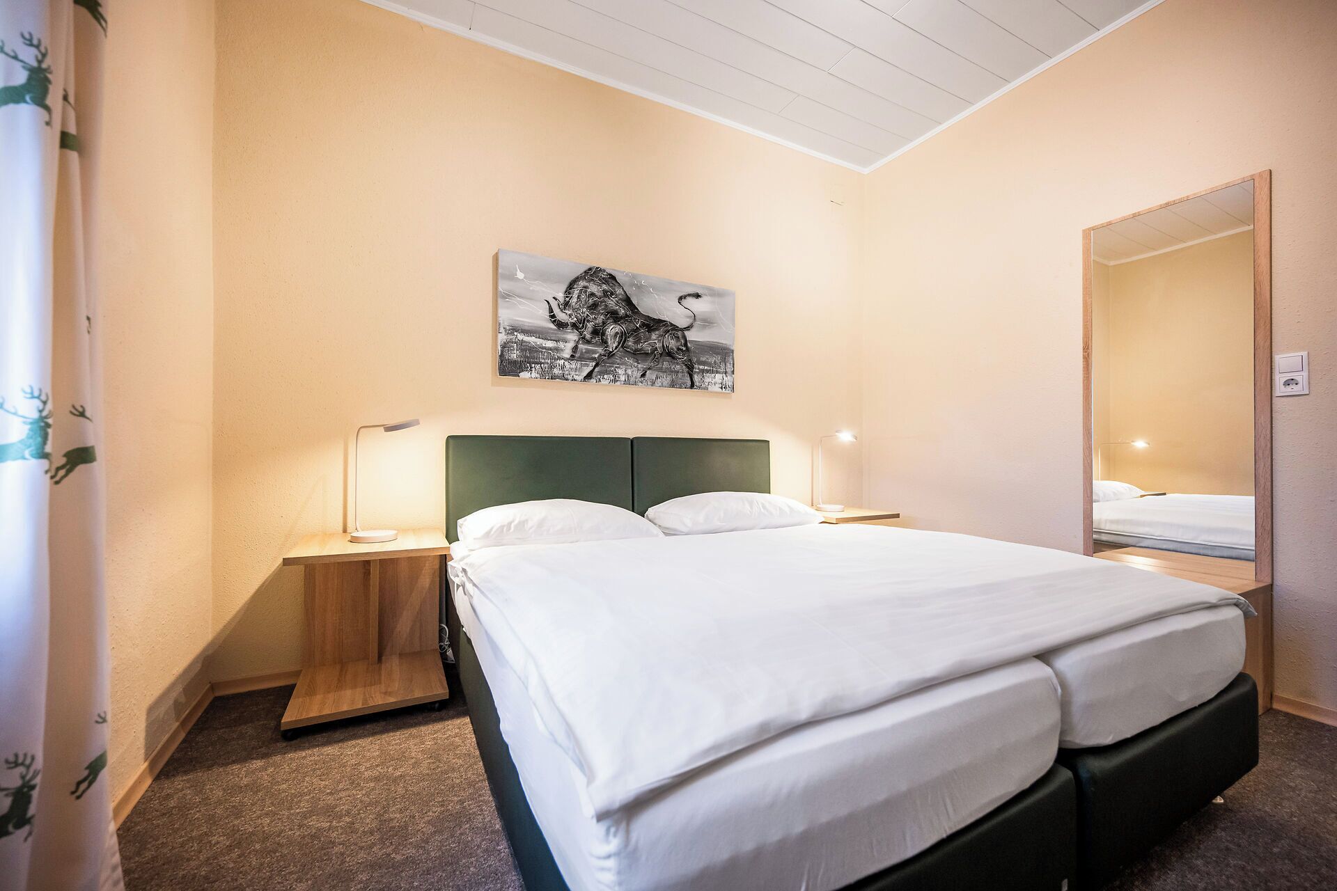 A hotel room with a bed, a nightstand, a lamp, a painting, and a mirror.