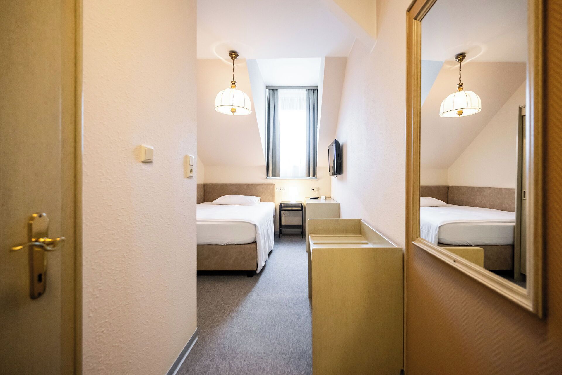 Une chambre d’hôtel avec deux lits, un petit bureau, une télévision et un miroir.