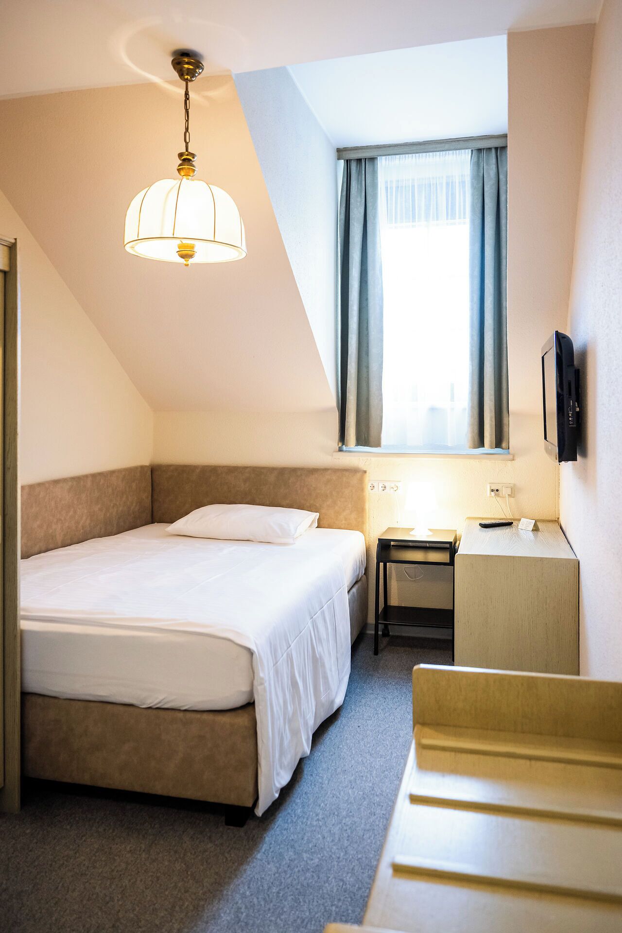 A hotel room with a bed, bedside table, and a desk with a chair.
