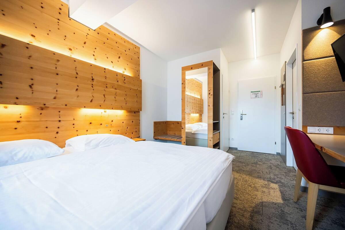 A hotel room with a wooden headboard, a bed, a desk with a chair, and a mirror.