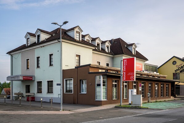 A multi-story building with a light blue and brown facade, featuring a prominent red sign for a hotel and a design studio.