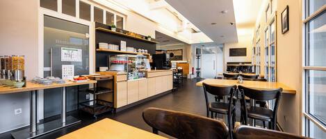 A modern restaurant with a central counter, seating area, and a kitchen in the background.