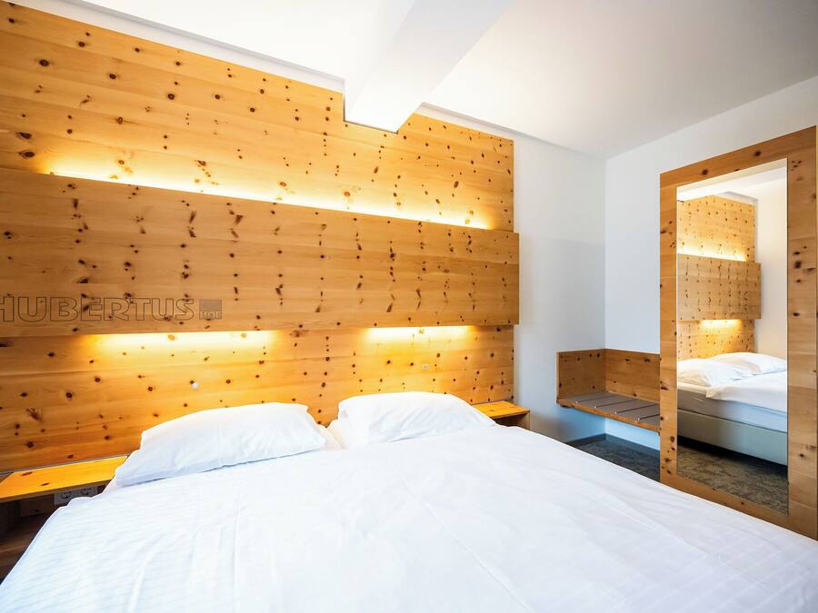 Un dormitorio con cabecera de madera, cama con ropa blanca, mesita de noche y espejo.