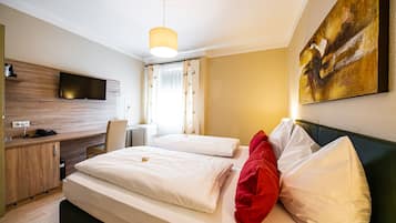 A hotel room with a bed, a desk, a chair, a TV mounted on the wall, and a painting on the wall.