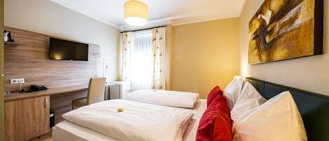 A hotel room with a bed, a desk, a chair, a TV mounted on the wall, and a painting on the wall.