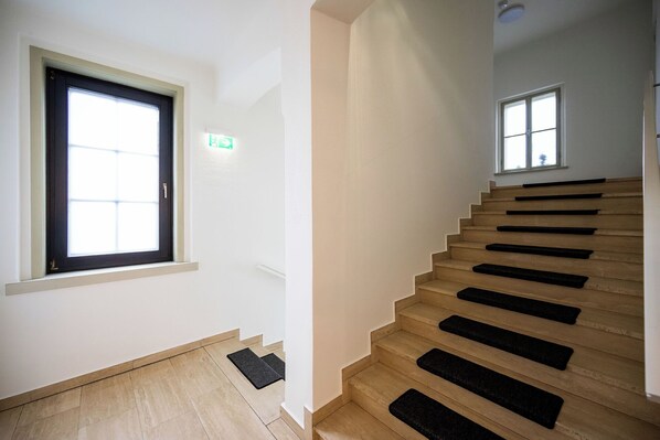 A staircase with wooden steps and black risers, a door with a window, and a small exit sign.