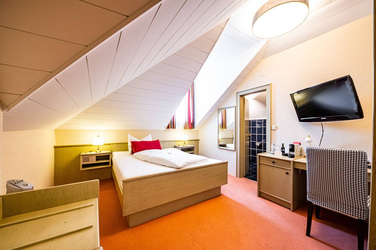 A hotel room with a bed, bedside tables, a desk, a chair, a television, and a bathroom door.