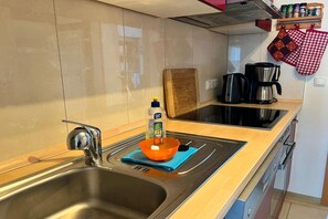 Eine Küche mit Edelstahlspüle, einer Holz Arbeitsplatte, einem Schneidebrett, einem Wasserkocher und einer Kaffeemaschine.