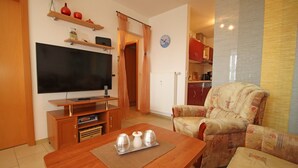 Una sala de estar con televisor, mueble de madera para entretenimiento, sofá y una mesa de comedor con mantel individual.