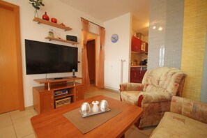 Ein Wohnzimmer mit Fernseher, einer Holzunterhaltungsecke, einer Couch und einem Esstisch mit Unterlage.