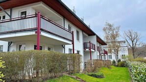 Un edificio residencial de dos pisos con balcones, un jardín y cielo despejado.
