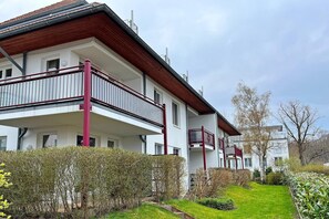 Ein zweistöckiges Wohngebäude mit Balkonen, einem Garten und blauem Himmel.