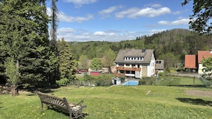 Eine Wiese mit einer Bank, ein Haus mit einem Balkon und ein Pool im Hintergrund.