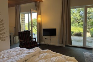 A bedroom with a large bed, a TV mounted on the wall, and a window with curtains.