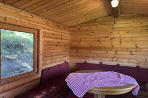 A wooden cabin interior with a round table and benches.