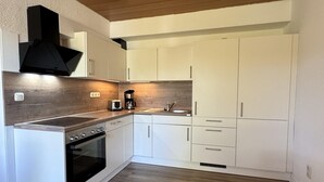 Eine moderne Küche mit weißen Schränken, einem eingebauten Backofen, einer Kaffeemaschine und einer Holzrückwand.