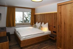 Ein Schlafzimmer mit einem hölzernen Bett, einem fenster mit Vorhängen, einem Kleiderschrank und einem Nachttisch.