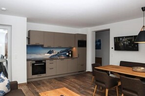 A modern kitchen with grey cabinets, a wooden dining table, and a painting of a mountain landscape. - Apartment in Bramberg near Cable Car (Bramberg am Wildkogel)