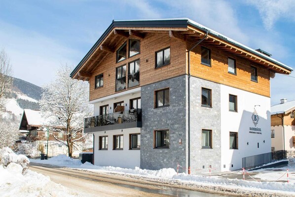 Ein mehrstöckiges Hotel mit Holzfassade und einem Steinwand-Akzent, mit Balkonen und Blick auf eine Skipiste.