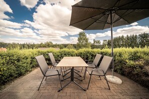 An outdoor patio with a table and chairs, surrounded by greenery and a clear sky.