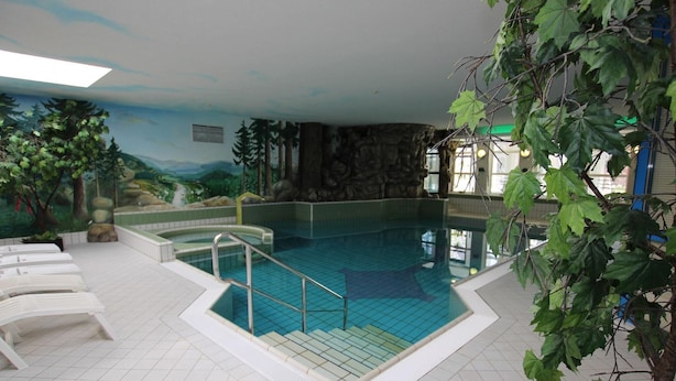An indoor swimming pool with a mural of a forest scene, a stone wall, and a tiled floor.