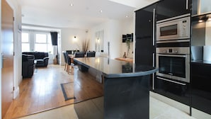 Eine moderne Küche mit Kochinsel, Edelstahlgeräten und einem Essbereich mit schwarzem Sofa und Stühlen.