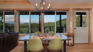 Un comedor con mesa, sillas y vistas a la montaña a través de amplios ventanales.