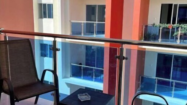 Un balcon avec deux chaises et une petite table, donnant sur un immeuble à la façade rouge et blanche.