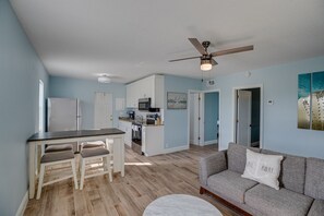 A modern kitchen with white cabinets, a dining table with two chairs, and a ceiling fan.