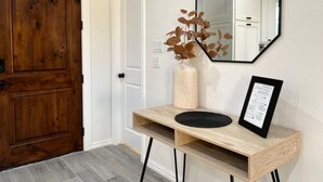Eine Holztür, eine weiße Tür, ein Spiegel, eine Vase mit Blättern und ein gerahmtes Zertifikat auf einem Holzkonsolentisch.