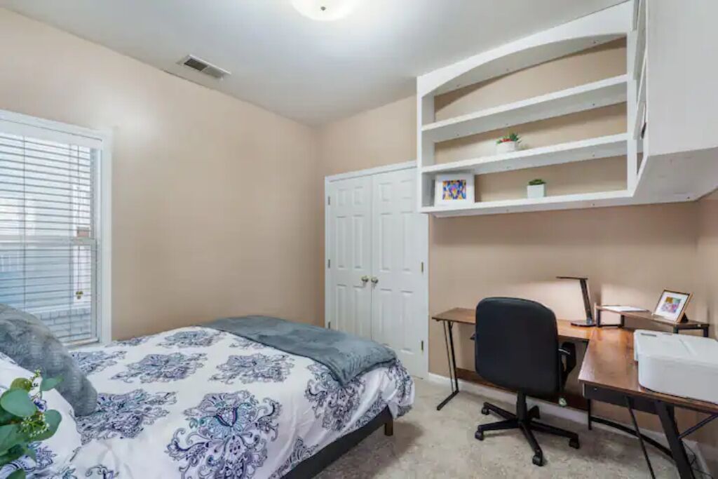A bedroom with a bed, a desk, and a shelving unit.
