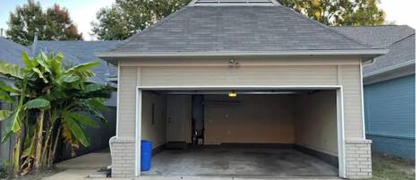 Une maison de plain-pied avec un garage, une cheminée en briques et un grand arbre dans le jardin.