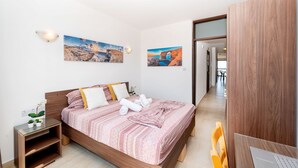 A modern bedroom with a wooden bed, two wall-mounted paintings, a bedside table with a lamp, and a laptop on a desk. - Sea Bliss Penthouse with two terraces enjoying side seaviews by Gatewaysmalta (St. Paul's Bay)