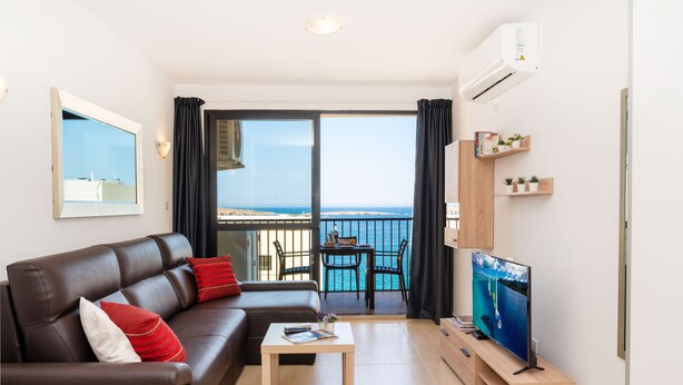 A modern living room with a leather sofa, a coffee table, a TV on a wooden stand, and a balcony with a view of the sea. - Sea Bliss Penthouse with two terraces enjoying side seaviews by Gatewaysmalta (St. Paul's Bay)