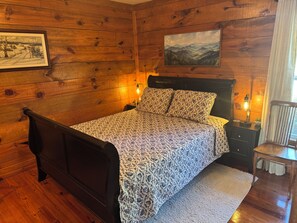 A wooden-paneled room with a bed, a nightstand, a lamp, and a framed picture on the wall.